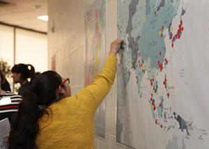 A woman placing a marker on a wall map of Asia that shows where the participants come from.